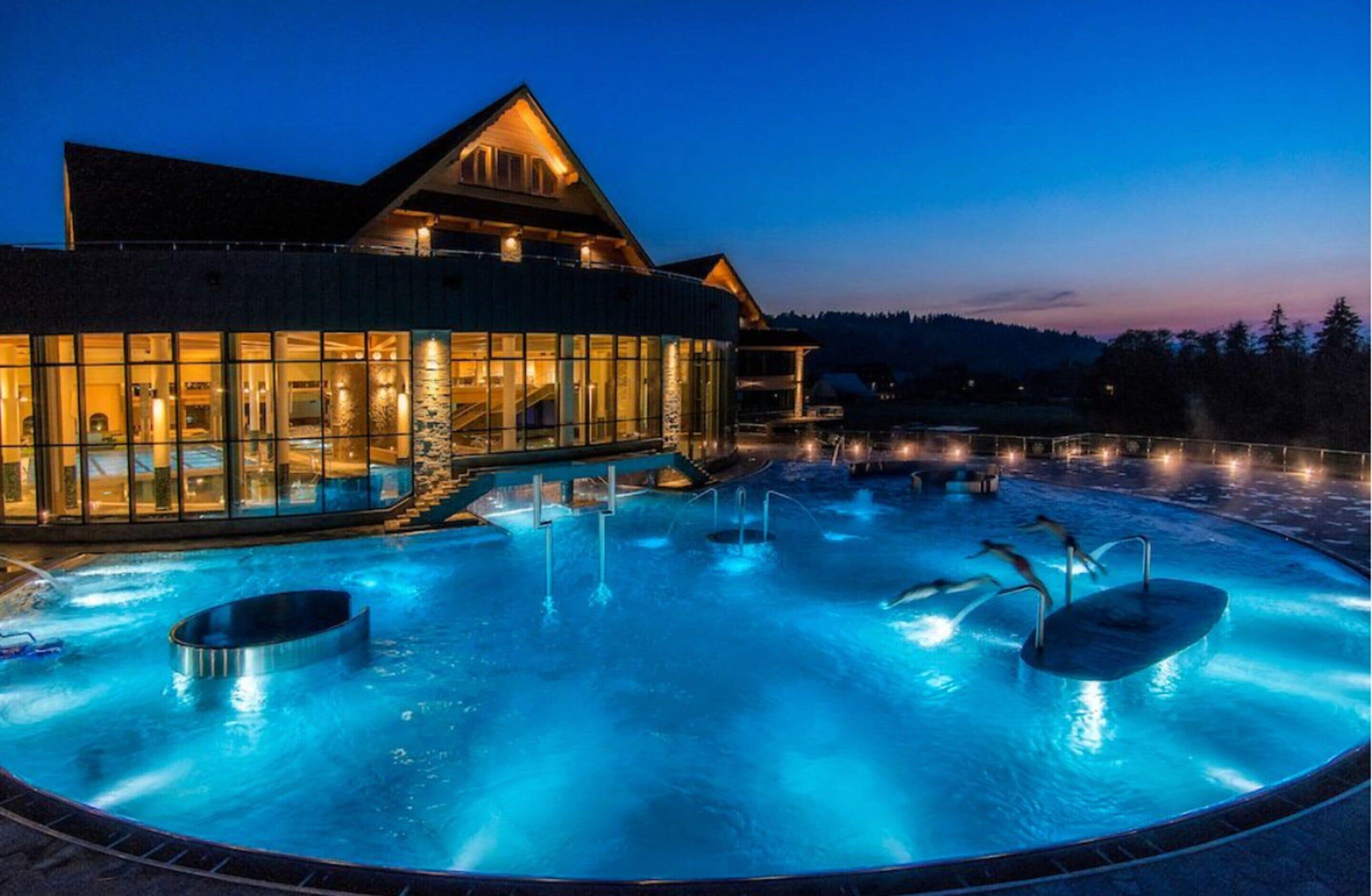 A hotel with a large outdoor heated pool area, a building with large windows, and a mountainous backdrop.