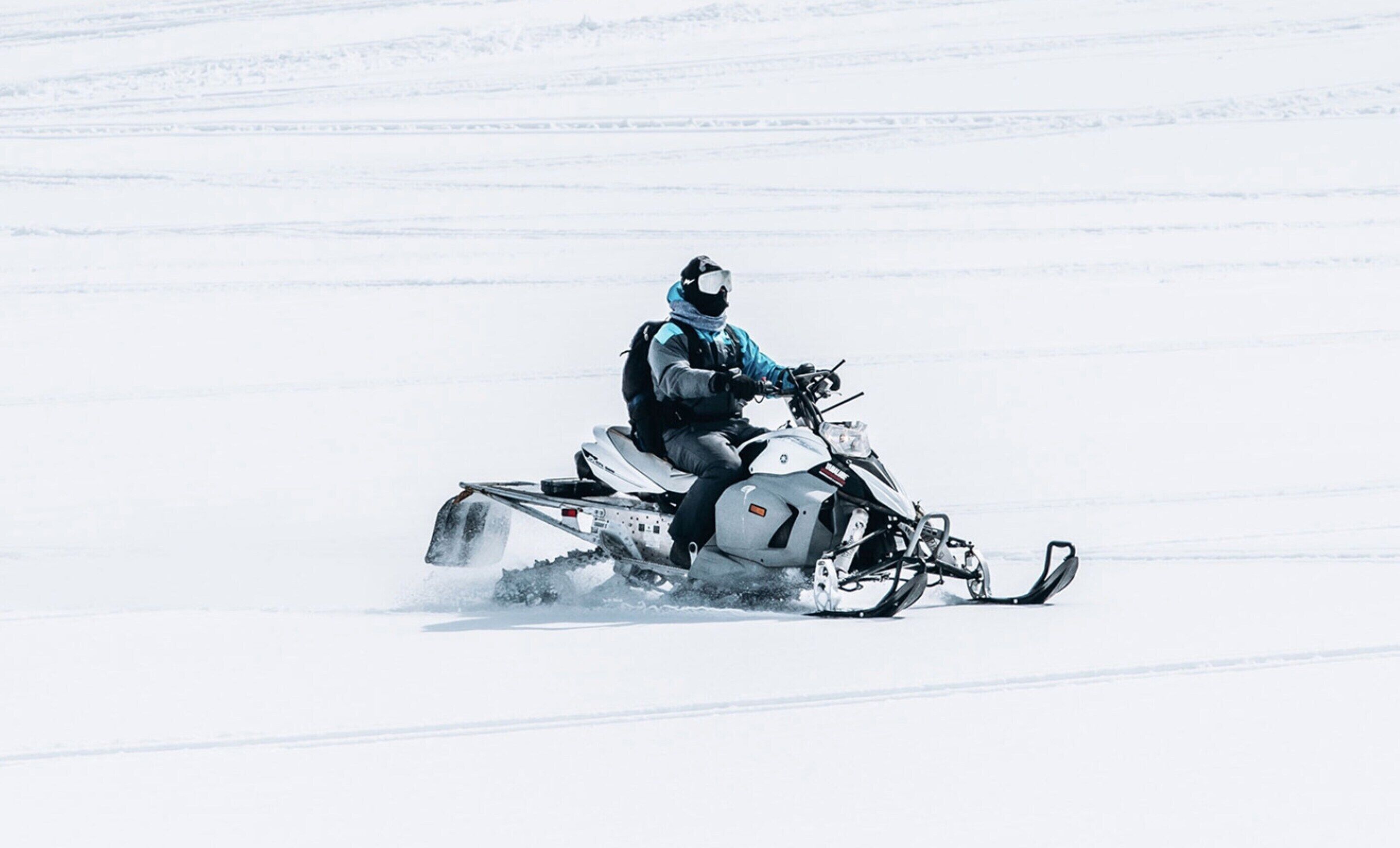 Un motoslitta con un guidatore su una superficie nevosa e pianeggiante.