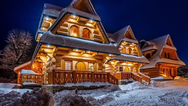 A large, multi-story log cabin with a steeply pitched roof, illuminated windows, and a snow-covered exterior. - Two-story Mountain-style House, Sauna, Jacuzzi (Poronin)