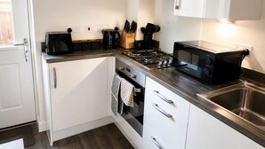 Una cucina compatta con piano cottura a gas, microonde, tostapane e una sveglia appesa al muro.
