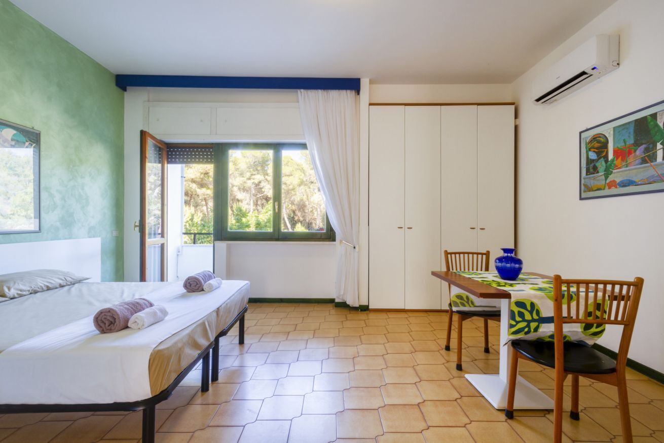 Een kamer met een bed, een tafel met stoelen, een raam met gordijnen en een airconditioning.