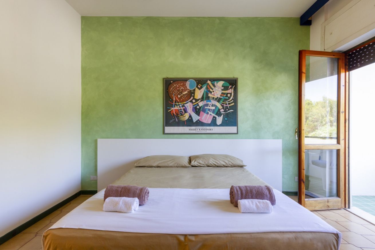 A double bed with two towels, a green wall, and a framed abstract painting.