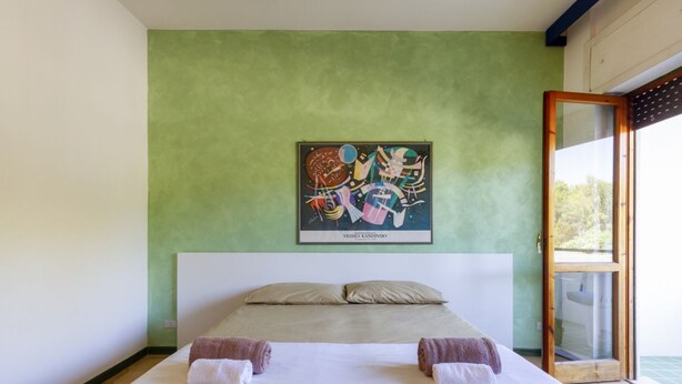 Een tweepersoonsbed met twee handdoeken, een groene muur en een lijst met een abstract schilderij.