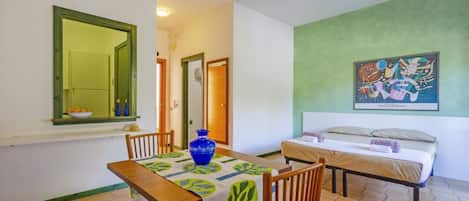 Una habitación con cama, una mesa con sillas, un jarrón y un cuadro en la pared.