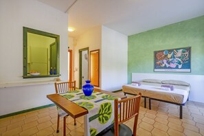 A room with a bed, a table with chairs, a vase, and a painting on the wall. - A cozy studio apartment with a balcony and kitchenette—perfect for two—located within the Campoverde Residence in Vernole, set in a Mediterranean pine forest between San Cataldo and the Le Cesine Nature Reserve. The property is just a short distance  (Vernole)
