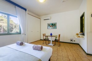 Une chambre d’hôtel avec un lit, une petite table avec des chaises, une fenêtre avec des rideaux et un climatiseur fixé au mur.