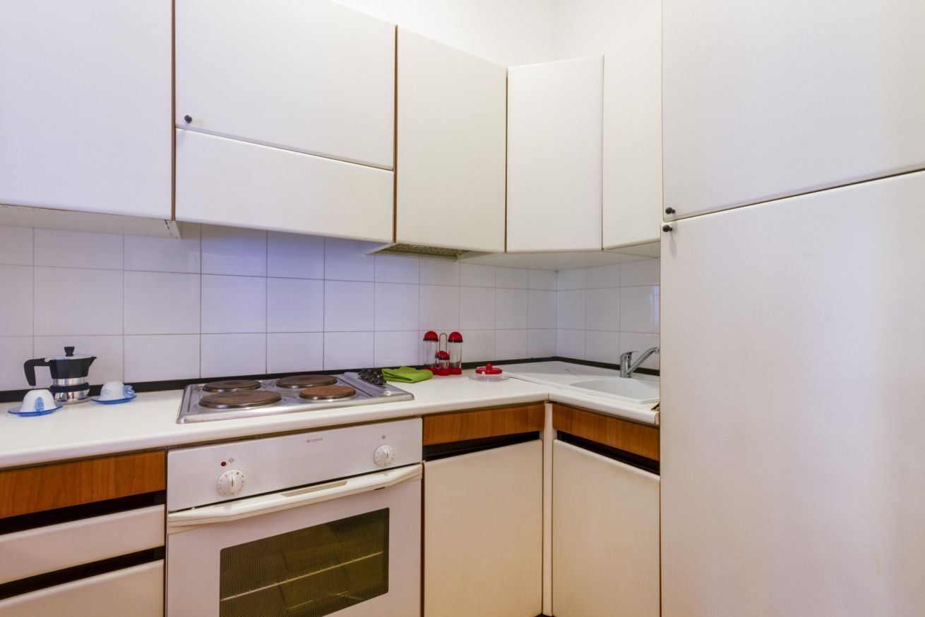 Una cocina compacta con gabinetes blancos, estufa, pileta y refrigerador.