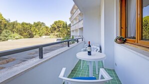 Een balkon met een tafel en stoelen, een fles wijn en een raam met een bloemenmand.
