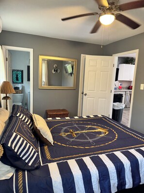 Une chambre avec un lit, un ventilateur de plafond, un miroir, une porte et un coin cuisine.