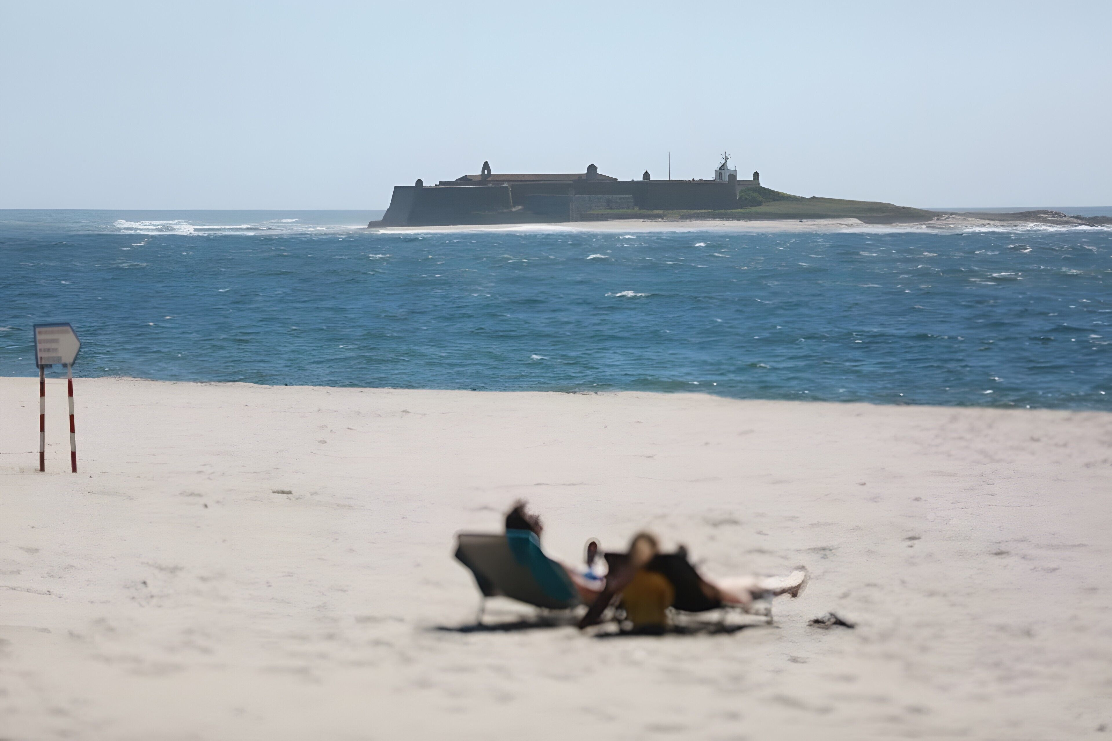 A beach with a large ship in the background and a lifeguard stand on the sand.