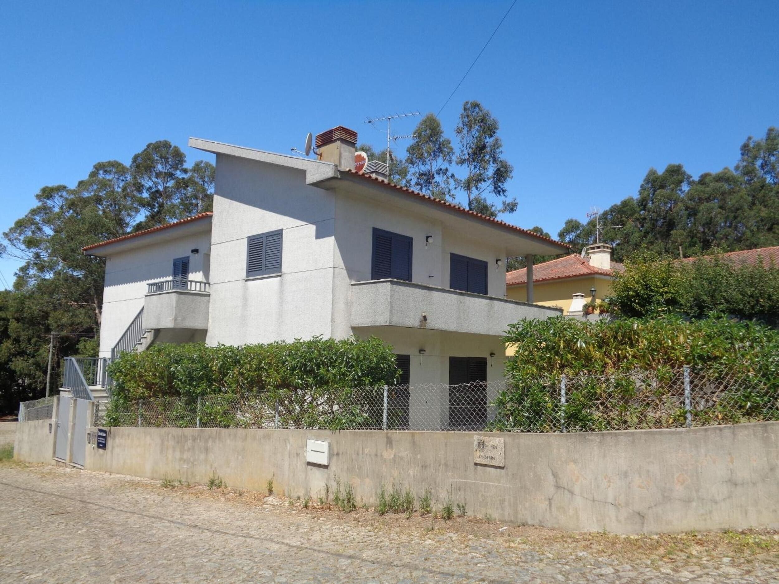 A two-story building with a balcony on the upper floor, a satellite dish on the roof, and a concrete wall in front.