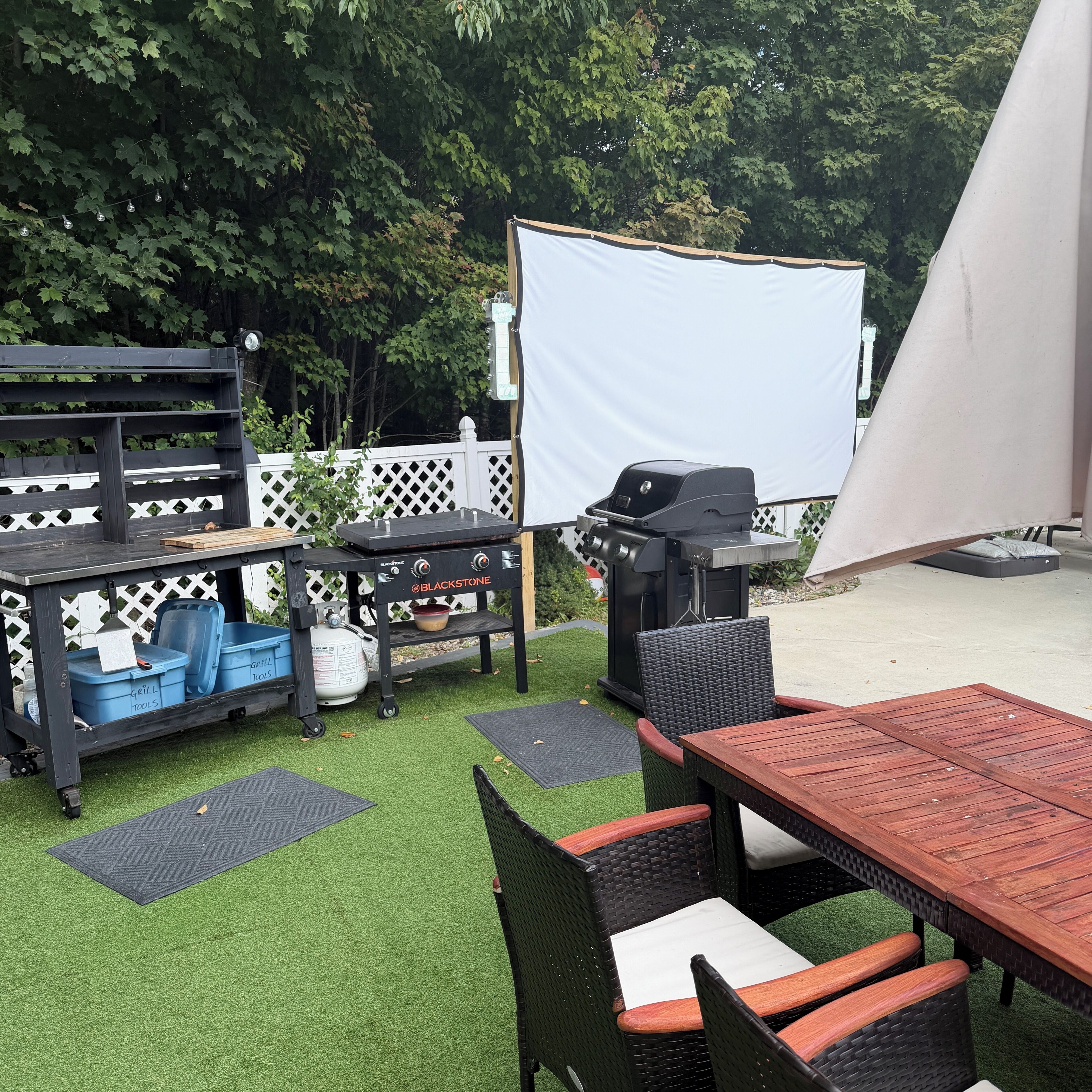 An outdoor patio with a grill, seating, and a white screen.