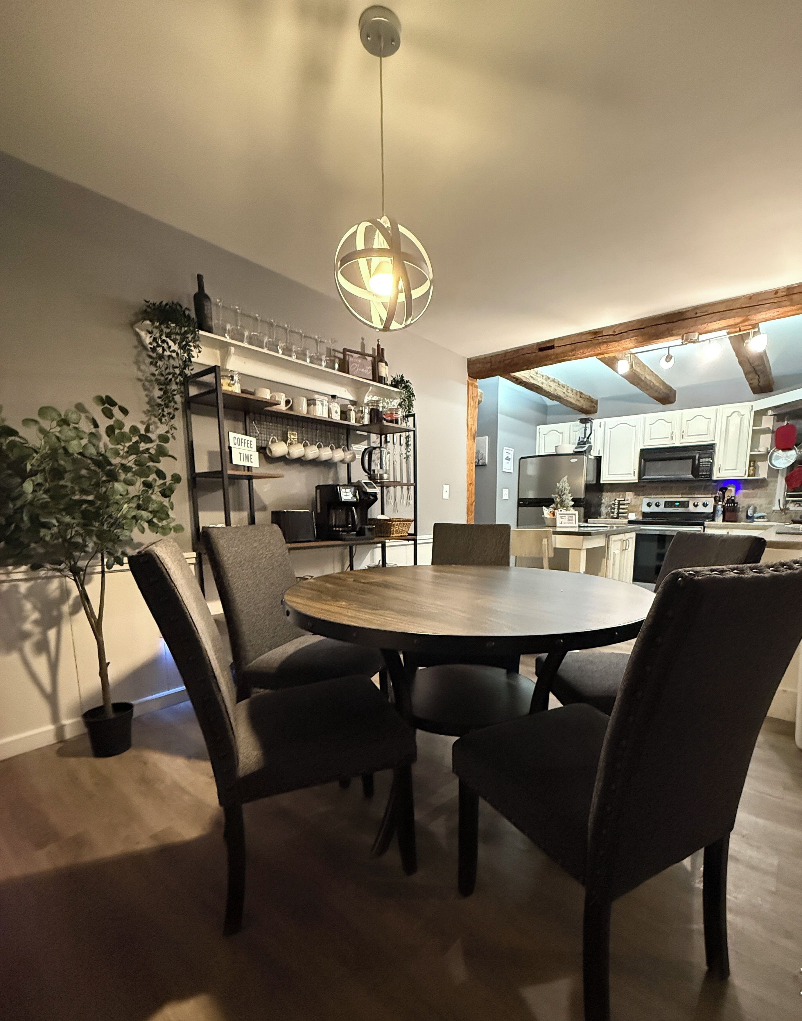Un coin repas avec une table ronde et des chaises, un luminaire suspendu et une cuisine en arrière-plan.
