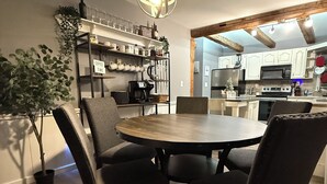 Uma área de refeições com uma mesa redonda e cadeiras, um lustre pendurado e uma cozinha ao fundo.