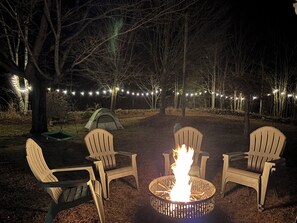 A nighttime outdoor setting with a fire pit, two chairs, and a tent.
