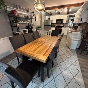 Zona pranzo con tavolo e sedie in legno, cucina sullo sfondo e tappeto decorativo sul pavimento.