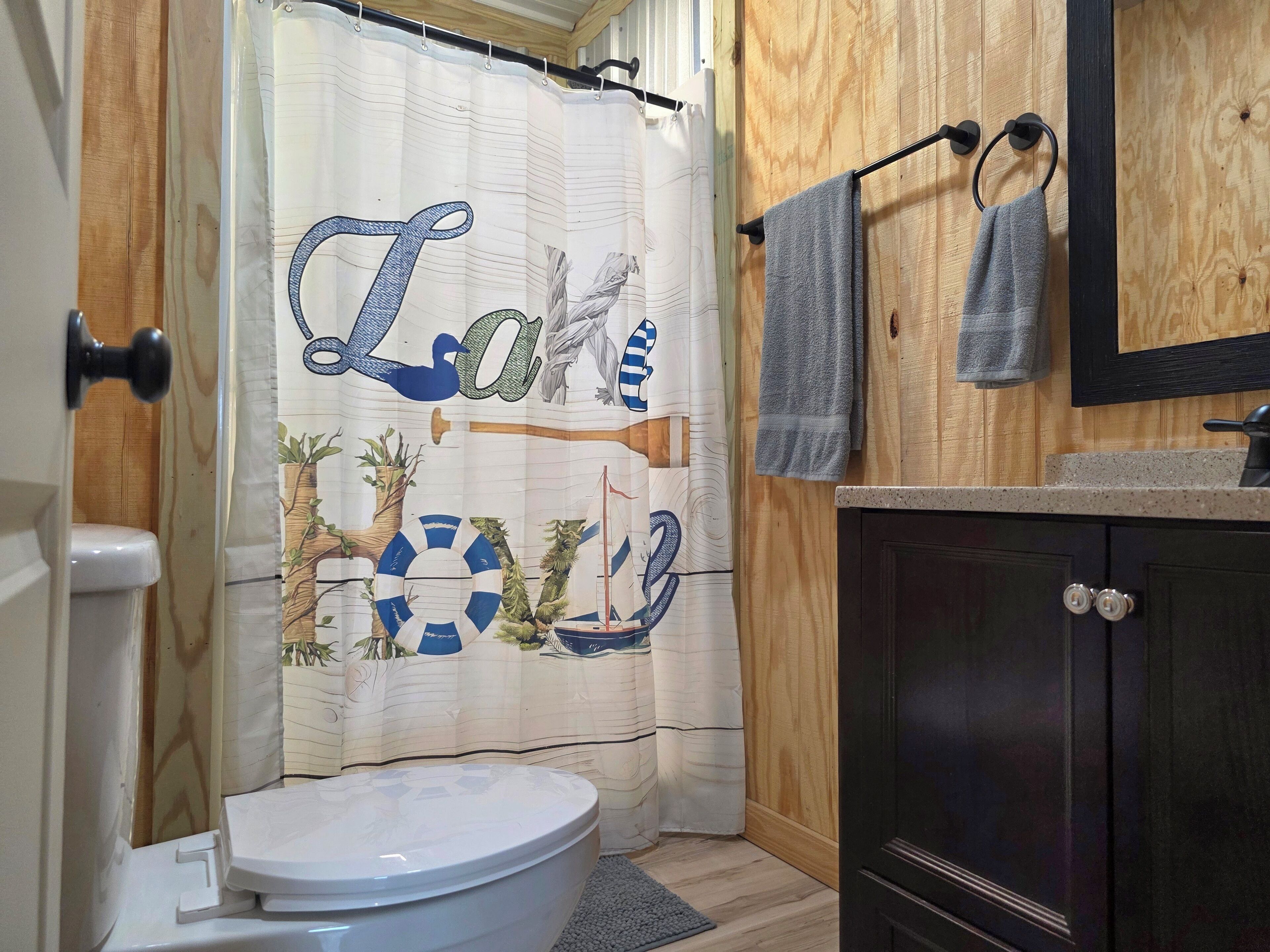 A bathroom with a toilet, a shower curtain with nautical designs, and a towel rack with towels.