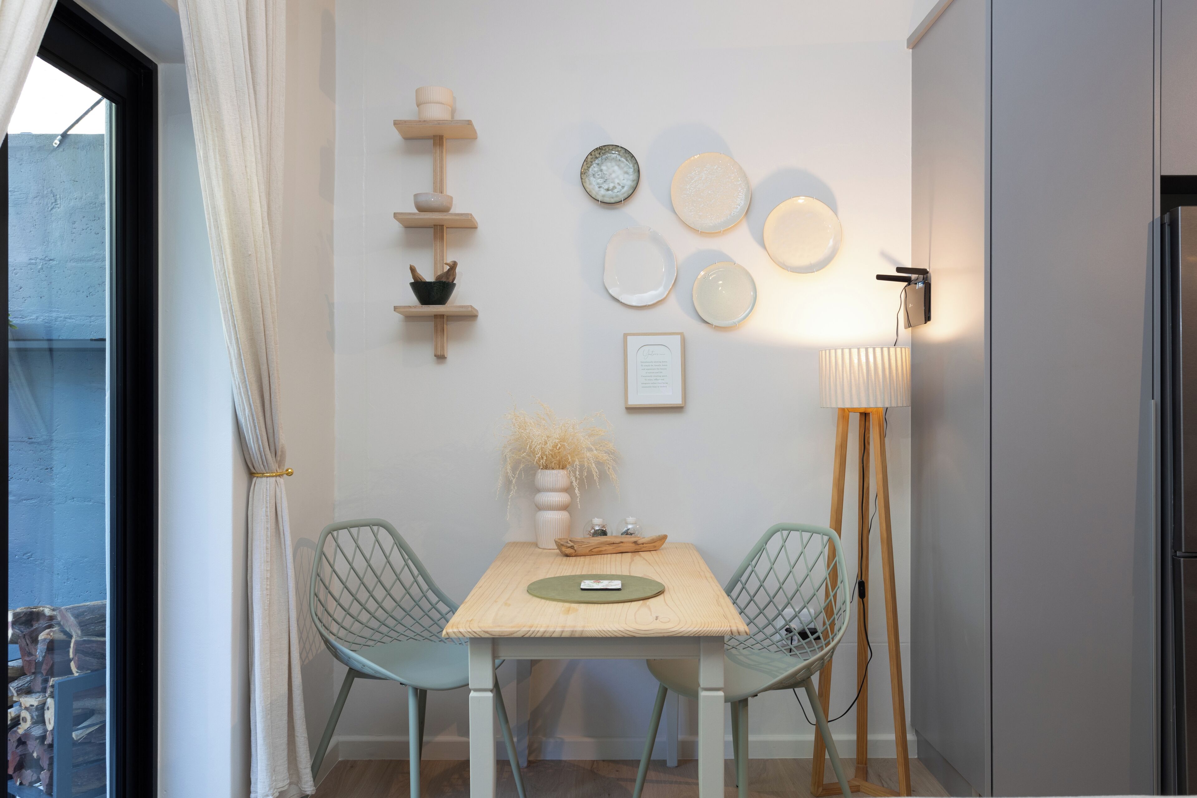 A dining area with a table, two chairs, a vase with dried plants, and wall-mounted plates.