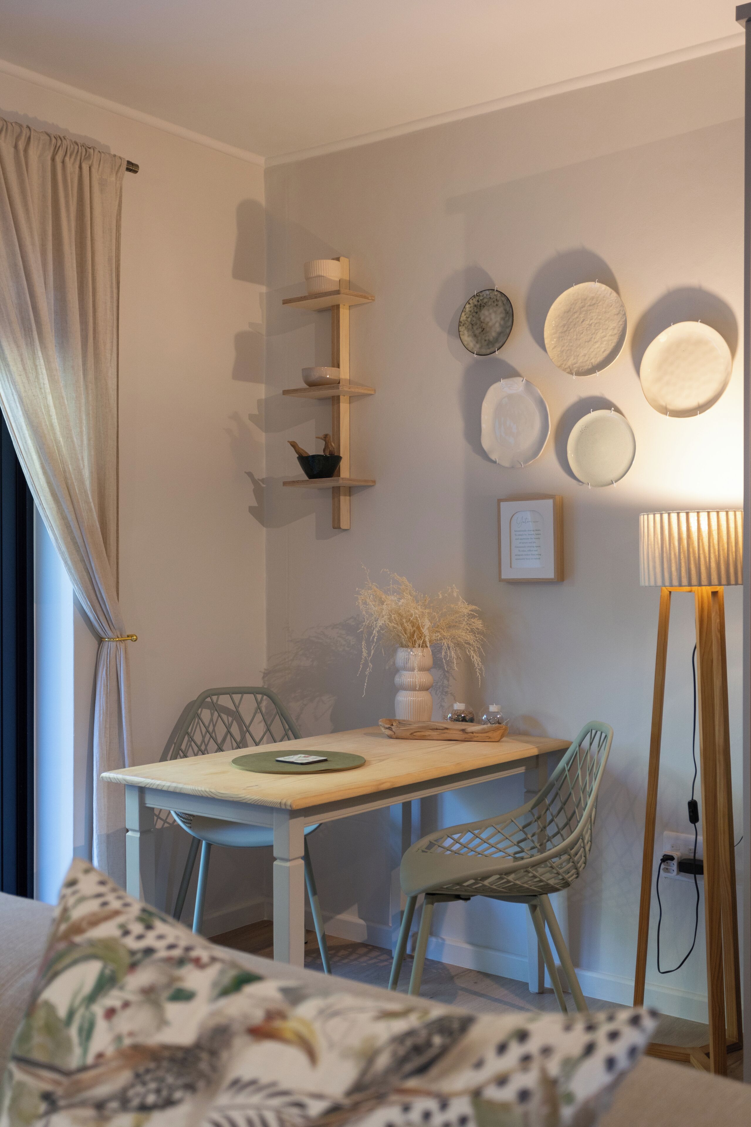 Un coin repas comprenant une table, des chaises, un vase contenant des plantes séchées et des assiettes décoratives accrochées au mur.