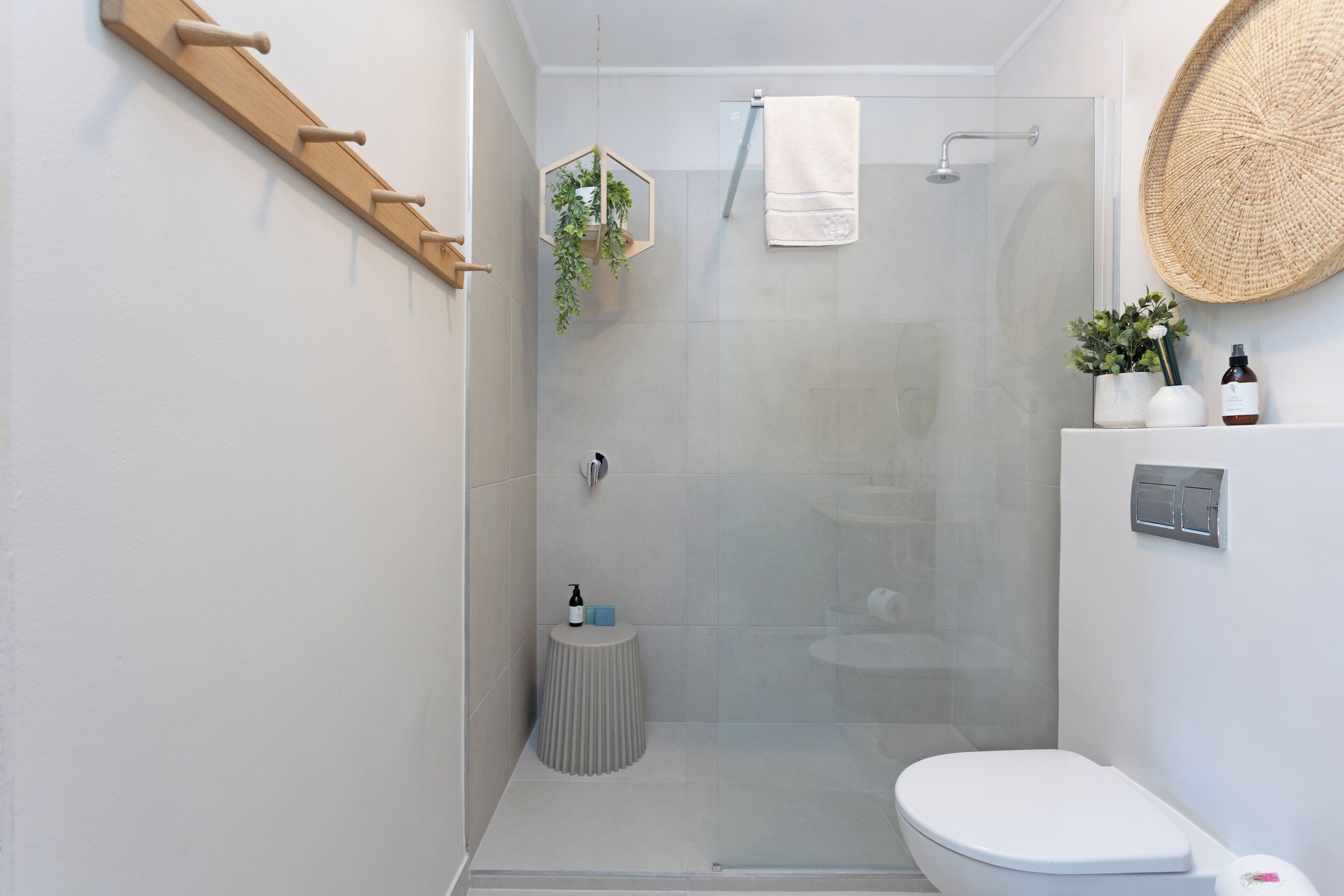 Et moderne badeværelse med et brusekabine i glas, et hvidt toilet og en lille, rund skammel.