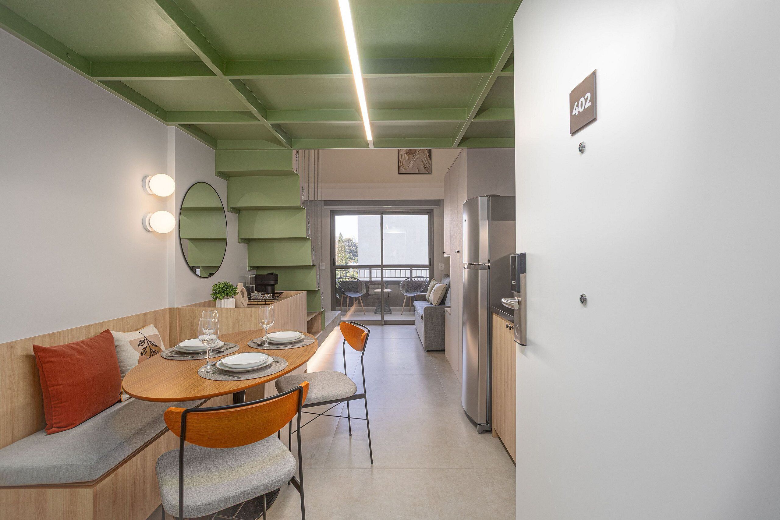 Une cuisine moderne dotée d’un réfrigérateur encastré, d’un coin repas avec une table et des chaises en bois, et d’un plafond vert.