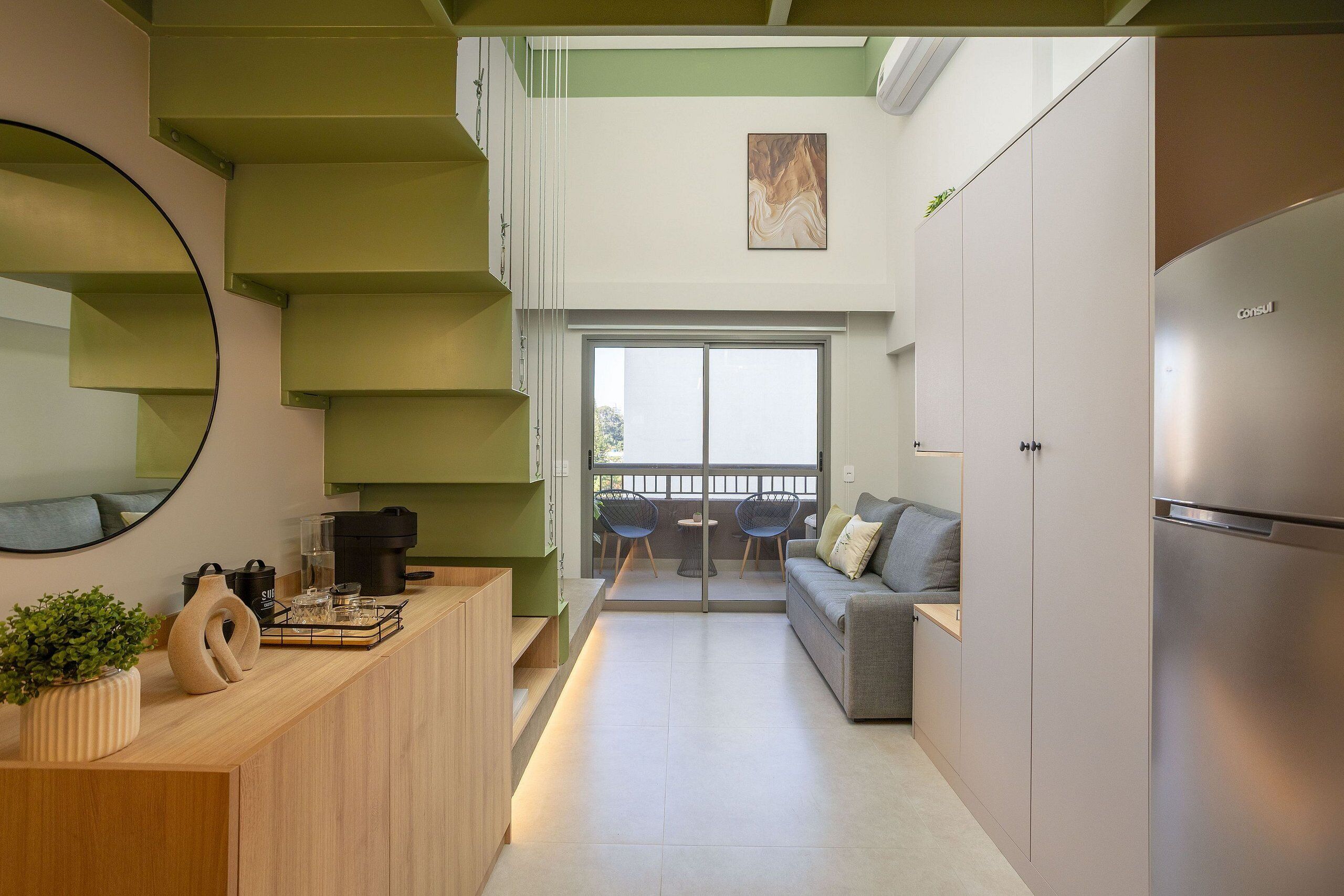 A modern kitchen with a built-in refrigerator, a dining area with a table and chairs, and a staircase with green steps.