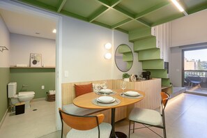 A modern kitchen with a dining area, featuring a round wooden table with chairs, a built-in oven, and a green accent wall. - Highlights Pinheiros (São Paulo)