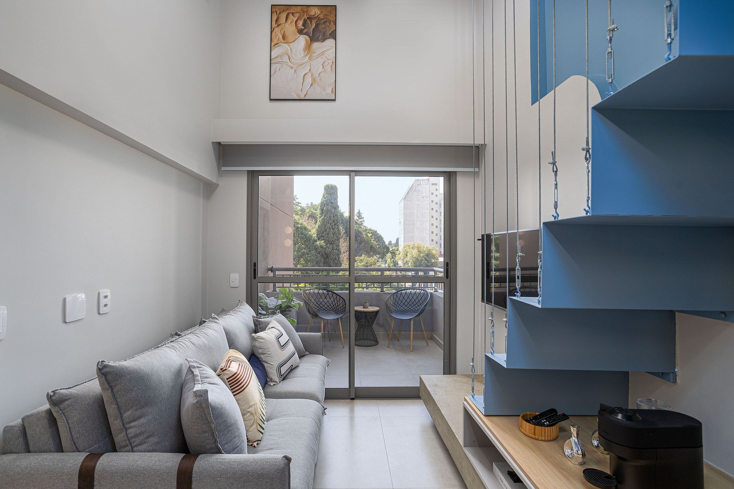 Un salon moderne avec un canapé gris, un téléviseur à écran plat et un balcon agrémenté de mobilier d’extérieur.