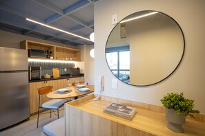A modern kitchen with a built-in oven, microwave, and a dining area with a round mirror, a telephone, and a magazine on the counter. - Highlights Pinheiros (São Paulo)