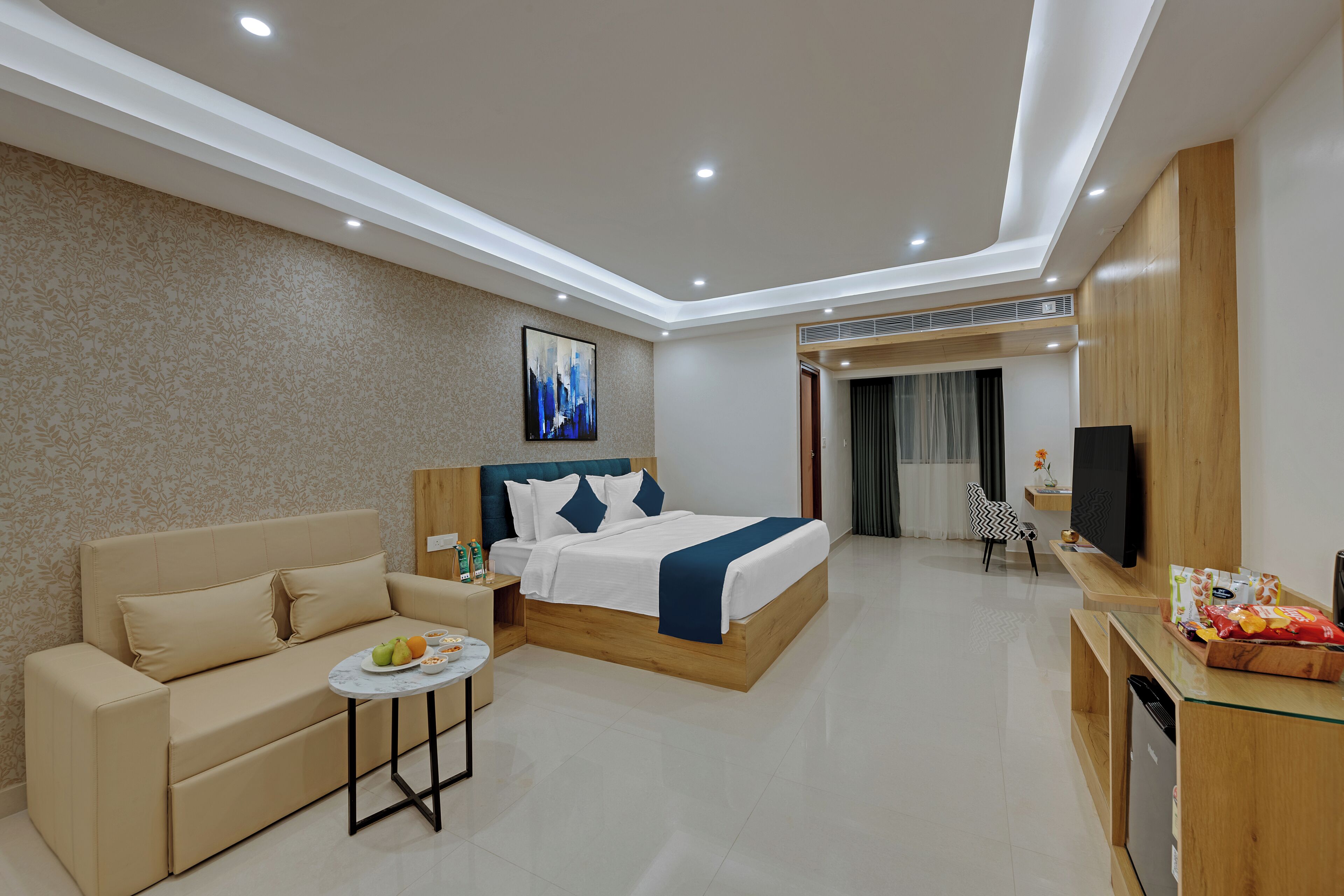 Una habitación de hotel moderna con una cama, un sofá, una mesita con fruta y un televisor.