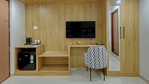 Una camera compatta con parete in legno, una TV a schermo piatto sopra un tavolino, un frigorifero e una sedia con rivestimento decorato.