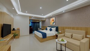 Una habitación de hotel moderna con una cama, un sofá, un televisor y una mesita con un florero y manzanas.