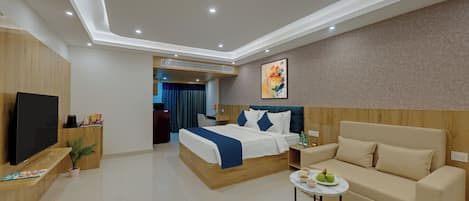 A modern hotel room with a bed, a sofa, a TV, and a small table with a vase and apples.