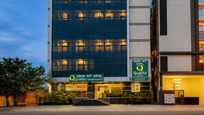 Un moderno edificio di hotel con facciata in vetro, insegna con la scritta 'Quality Inn Bhavishya' e un ingresso visibile con gradini.