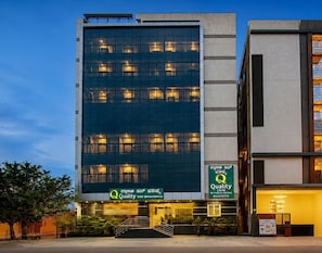 Un moderno edificio de hotel con fachada de vidrio, señalización que dice 'Quality Inn Bhavishya' y una entrada visible con escalones.