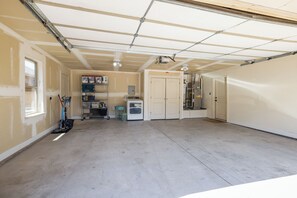 Un garage avec un sol en béton, un lave-linge et une étagère contenant divers objets.