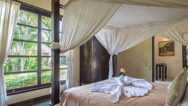 Quarto com cama, janela com cortinas, mesa de cabeceira e um quadro na parede.