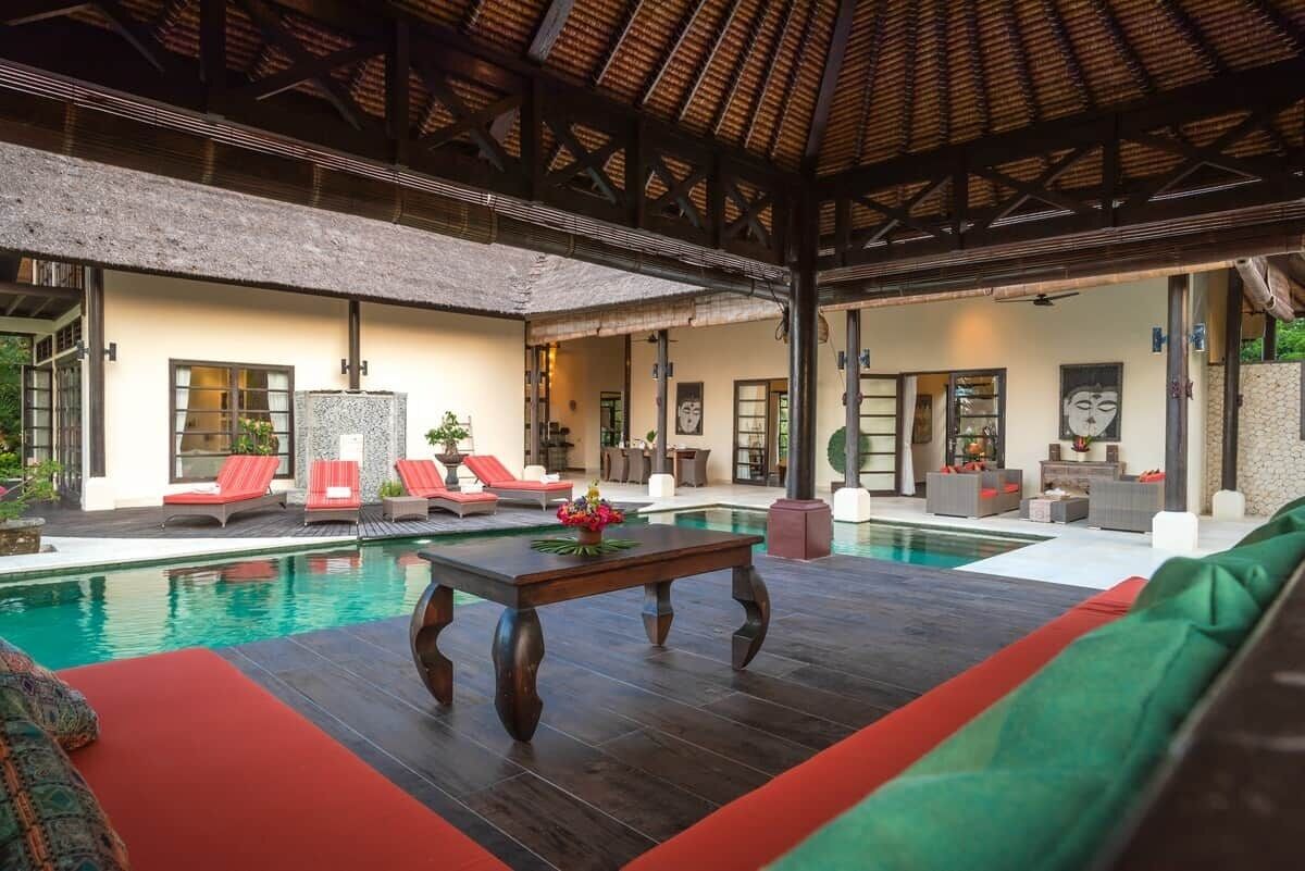 Area piscina con lettini, un tavolo in legno e una zona relax coperta.