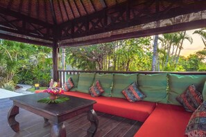 A covered outdoor seating area with a wooden table and colorful cushions.