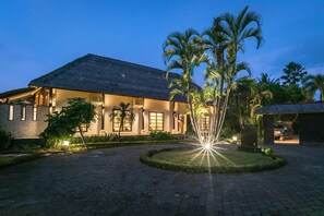 A building with a thatched roof, surrounded by a paved courtyard with palm trees.
