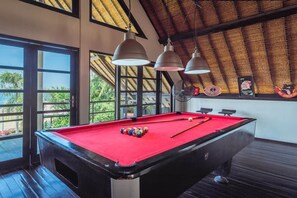 Ein Billardtisch mit Kugeln, Deckenbeleuchtung und Blick durch große Fenster.