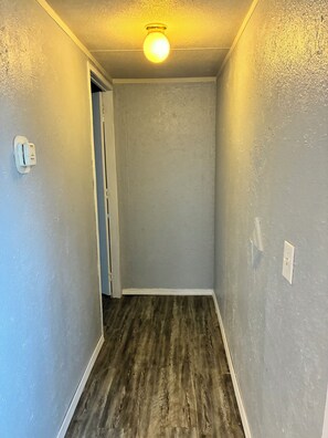 Un pasillo estrecho con piso de madera, paredes de color gris claro y una lámpara en el techo.