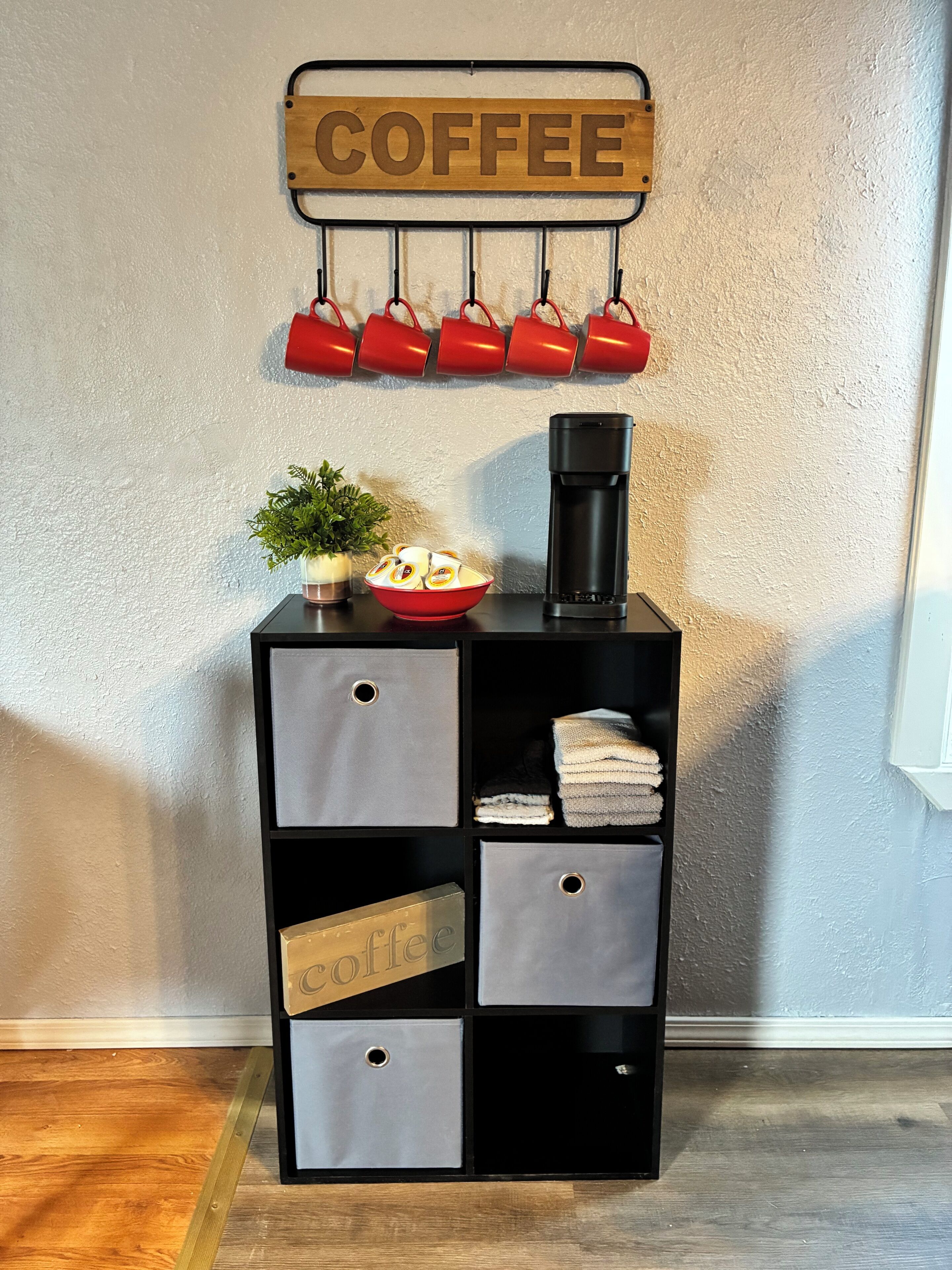 Un depósito para almacenamiento negro con un letrero alusivo al café, una cafetera y un tazón de cápsulas de café.