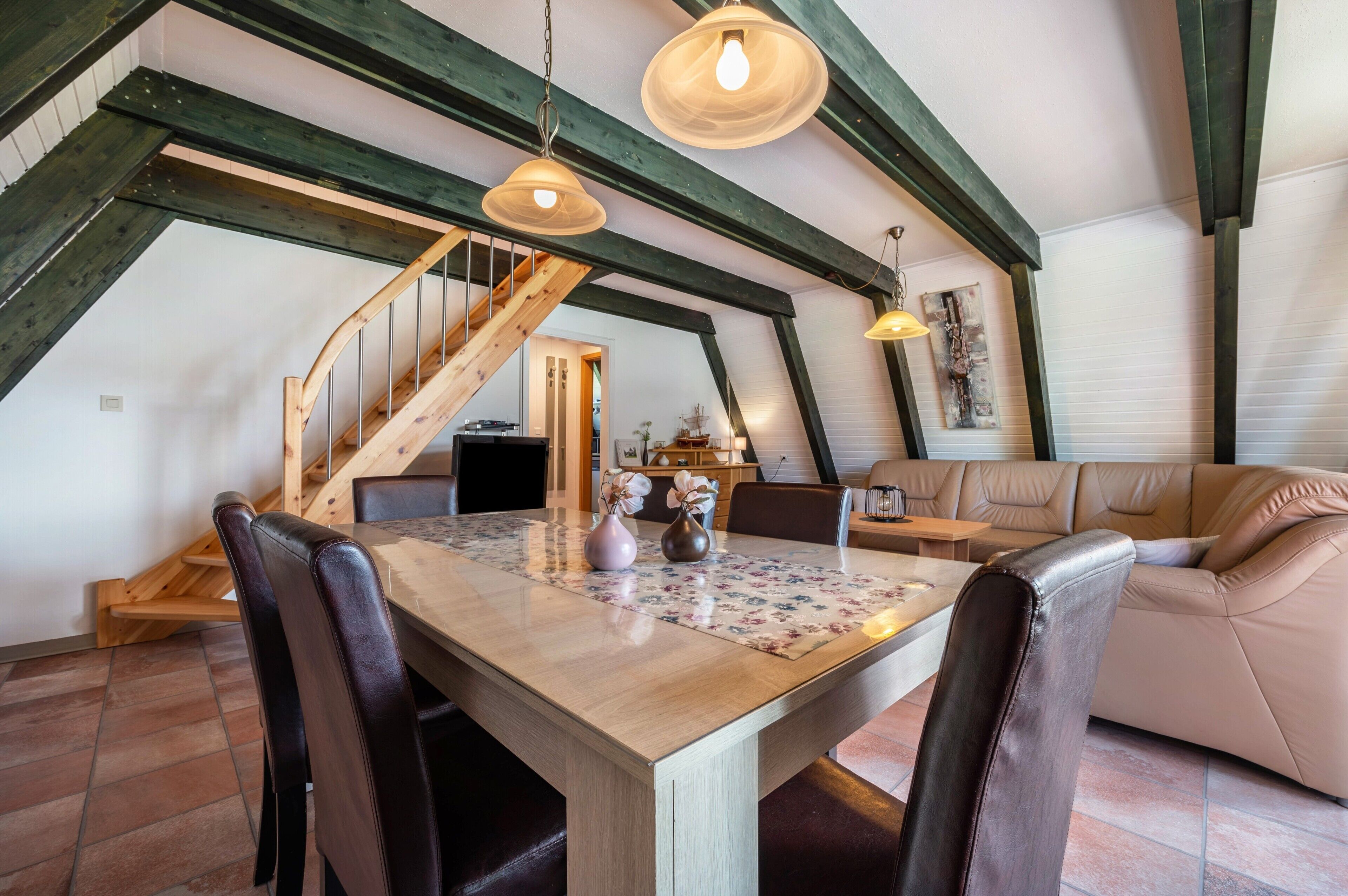 Ein Essbereich mit Holztisch, Stühlen und einer Treppe mit freiliegenden Balken.