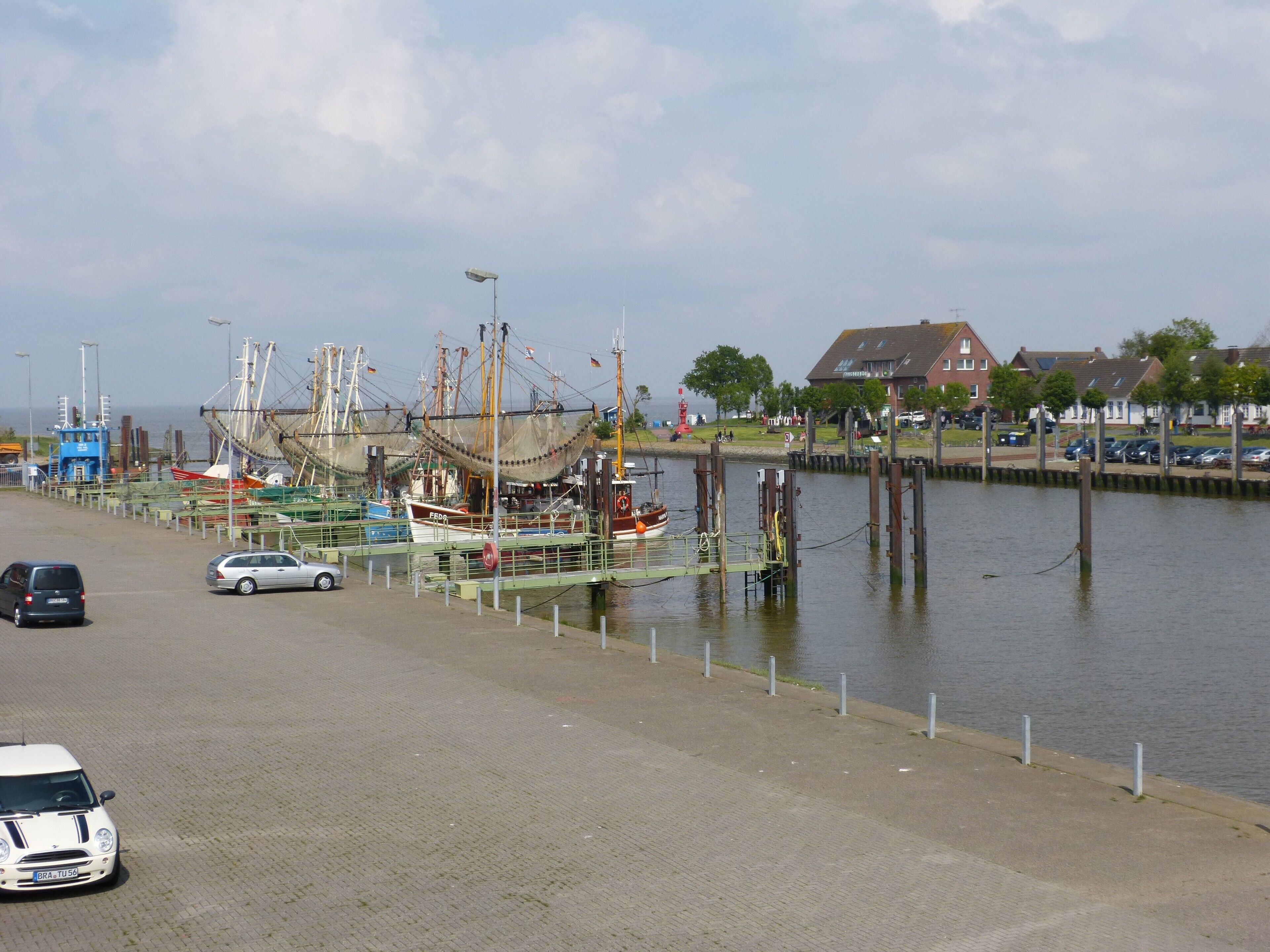 Ein Hafen mit vor Anker liegenden Booten, eine Straße mit Autos und Gebäude im Hintergrund.