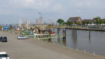 Ein Hafen mit vor Anker liegenden Booten, eine Straße mit Autos und Gebäude im Hintergrund.