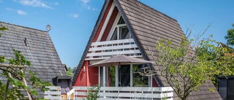Ett modernt hus med en röd fasad, ett sluttande tak och en balkong med ett vitt räcke.