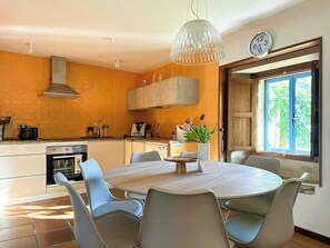 A modern kitchen with a round dining table, light-colored chairs, and a hanging light fixture. - Galician stone house with hórreo and garden (Bustelo)
