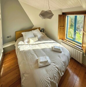 A bedroom with a large bed, a wooden headboard, a window with a view of greenery, and a hanging light fixture. - Galician stone house with hórreo and garden (Bustelo)
