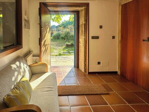 A room with a sofa, a wooden door, and a view of a garden through an open door. - Galician stone house with hórreo and garden (Bustelo)